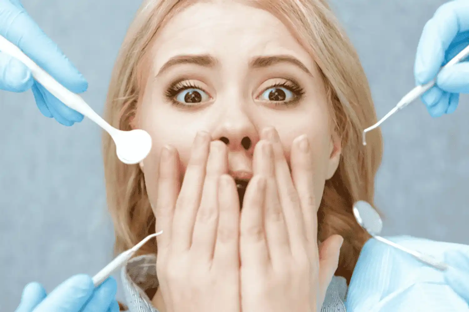 Vrouw ligt met een geschrokken gezicht in een tandartsstoel terwijl de tandarts gereedschappen bij haar mond houdt.